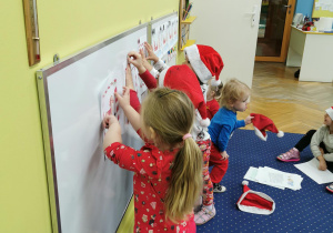Pomocnicy Świętego Mikołaja przyczepiają obrazki na tablicy.